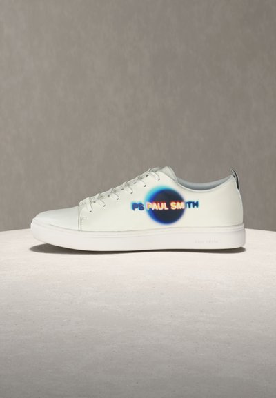 Baskets blanches basses avec lacets, arborant un logo flou multicolore "PS PAUL SMITH" sur un cercle noir sur le côté.