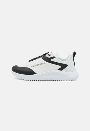 Baskets basses Calvin Klein blanches et noires avec semelle blanche, zone des lacets noire et texte "Calvin Klein Jeans" sur le côté.