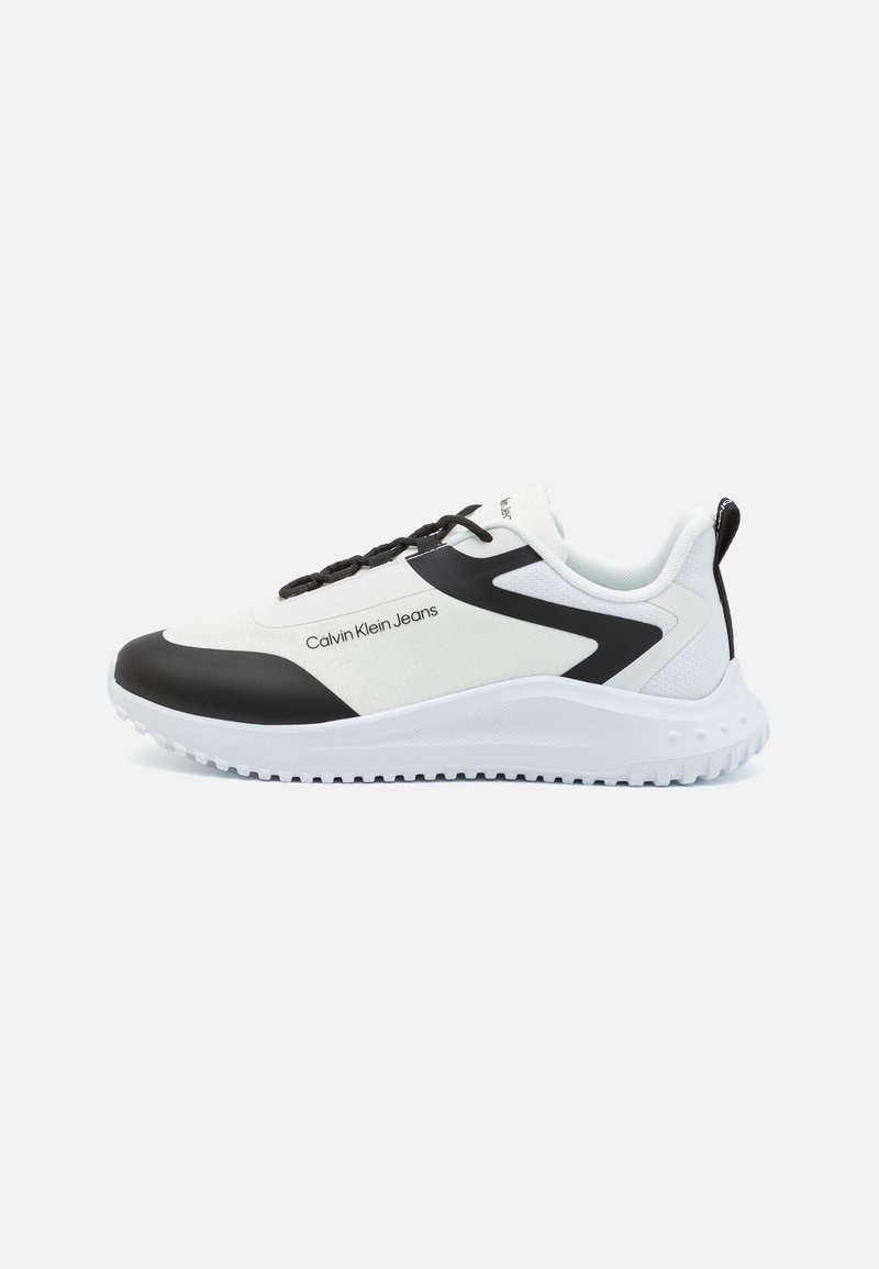 Baskets basses Calvin Klein blanches et noires avec semelle blanche, zone des lacets noire et texte "Calvin Klein Jeans" sur le côté.