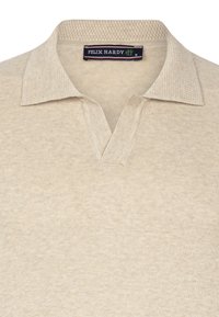 Beige Poloshirt mit texturiertem Kragen und V-Ausschnitt-Design. Hergestellt aus weichem Material mit einem dezenten Muster. Markenlabel sichtbar.