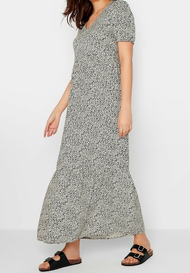 Czarna i biała maxi sukienka w kropki z krótkimi bufkami, dekoltem w serek i rozkloszowanym dołem. Modelka nosi czarne sandały z klamrami.