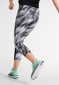 Czarno-białe legginsy capri z diagonalnym paskiem, połączone z miętowo-zielonymi butami sportowymi z teksturowanym wierzchem i białą podeszwą.