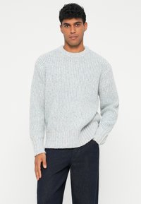 Maglione a maglia testurizzata grigio chiaro con un motivo a coste, scollatura rotonda e vestibilità comoda, abbinato a jeans blu scuro.