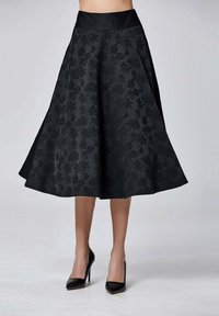 Jupe noire en A avec un motif floral, un tissu texturé et une large ceinture, assortie à des chaussures à talons hauts noires.