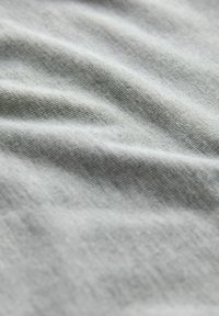 Ljust grått tyg med en mjuk, texturerad yta, som har mjuka vågor och veck, vilket indikerar ett lätt och luftigt material.