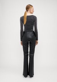 Schwarze, gefälschte Lederhose im Schlagstil, kombiniert mit einem formschönen, glitzernden Langarmoberteil. Glatte Textur und taillierte Passform, mit einer kleinen Tasche auf der Rückseite.