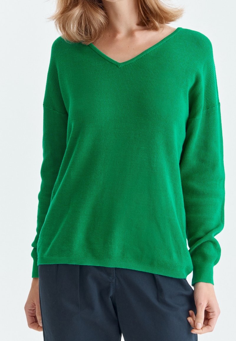 Pull en tricot vert avec un design en V, des manches longues, une texture côtelée et une coupe décontractée. Le tissu semble doux et légèrement extensible.