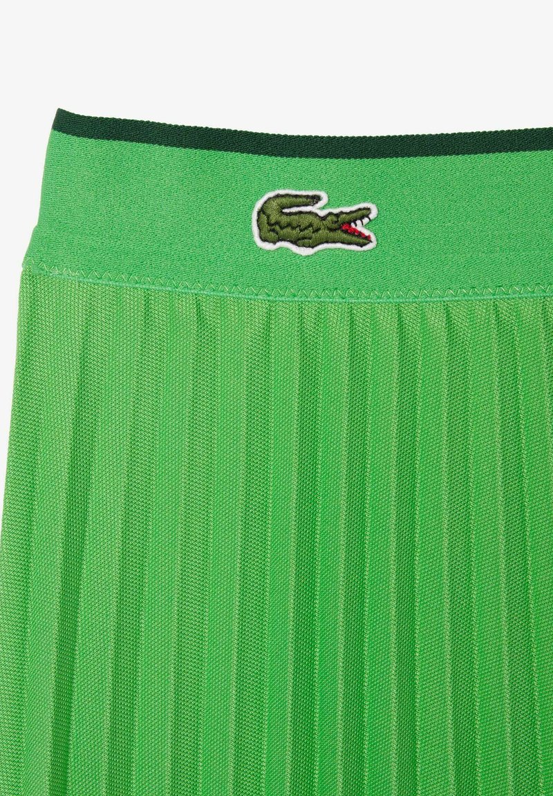 Zielona spódnica plisowana z pasem w ciemnozielonym kolorze i haftowanym logo krokodyla Lacoste na środku.