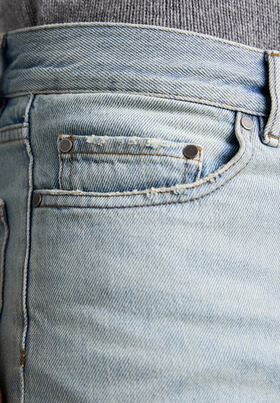 Jeans in denim azzurro chiaro con un design classico, che mostrano dettagli di cucitura, rivetti e una piccola tasca frontale. La texture appare leggermente usurata.