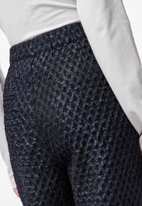 Pantaloni navy testurizzati con un sottile motivo in rilievo, vita elastica e vestibilità aderente, abbinati a un top di colore chiaro.