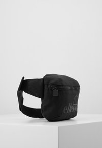 Sac à taille en tissu noir avec une fermeture éclair, doté d'un logo texturé sur le devant et d'une sangle ajustable pour un port sécurisé.