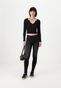 Černý dlouhý rukáv cropped top s henley výstřihem, zkombinovaný s přiléhavými černými džíny a černými teniskami s bílými akcenty. Zmíněná malá hnědá taška.