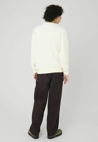 Pull crème avec des poignets et un ourlet côtelés, associé à un pantalon large marron foncé. Le pantalon a une texture lisse et une coupe décontractée.