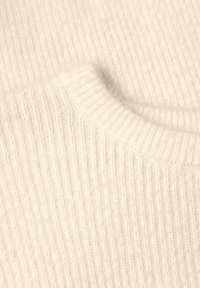 Gros plan sur l'encolure côtelée et le tissu en maille texturé d'un pull doux de couleur crème.