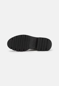 Suela de zapato de goma negra con ranuras horizontales para tracción, nombre de la marca en relieve y forma de punta redondeada. Acabado texturizado para mayor agarre.