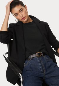 Czarna marynarka na czarnym swetrze, w połączeniu z niebieskimi dżinsami z wysokim stanem. Czarny pasek z klamrą w złotym odcieniu.