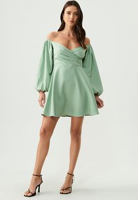 Mint zelena haljina s off-shoulder izrezom, pufastim dugim rukavima, uskim tijelom i raširenom suknjom, izrađena od glatkog, laganog materijala.