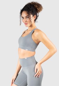 Szary sportowy stanik i szorty z wysokim stanem wykonane z gładkiego materiału, z minimalnym przeszyciem i brandingiem na pasie.