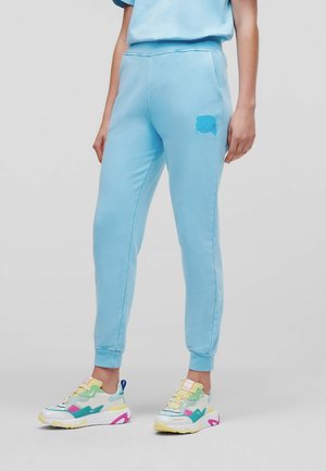 Jasnoniebieskie spodnie dresowe ze ściągaczami i małym logo na udzie, noszone z wielokolorowymi sportowymi butami.