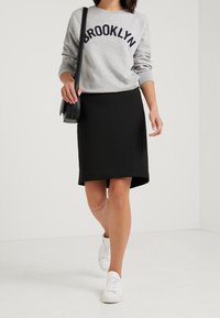 Šedá mikina s nápisem "BROOKLYN", doplněná černou sukní po kolena. Outfit doplňují bílé tenisky. Texturovaná tkanina; neformální styl.