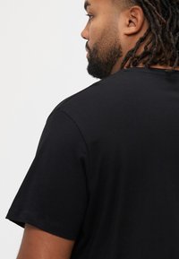 Μαύρο βαμβακερό T-shirt με κοντά μανίκια και στρογγυλή λαιμόκοψη. Ομαλή υφή και απλή σιλουέτα, εμφανιζόμενο από πίσω.