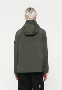 Jachetă ușoară de culoare verde închis, cu glugă. �Țesătură texturată cu aspect crăpat, cusături vizibile și manșete elastice. Design simplu și funcțional.