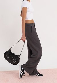 Pantalon gris à jambes larges avec plis devant, associé à un top blanc court et des baskets noires. Un sac à main noir avec des ferrures circulaires est tenu.
