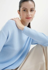 Maglione in maglia texturizzata di un blu chiaro, con maniche lunghe, vestibilità comoda e scollo a girocollo, abbinato a un pantalone drappeggiato di colore crema.