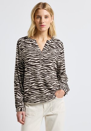 Chemise à rayures zèbre marron et crème à manches longues avec un décolleté en V et des poignets retroussés, associée à un pantalon beige clair. Texture de tissu lisse.