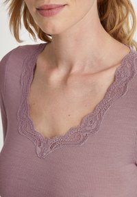 Paars geribbeld top met een diepe V-hals en verfijnde kantdetails langs de halslijn, die textuur en vrouwelijke ontwerpelementen accentueert.