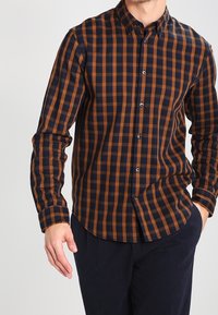 Chemise boutonnée avec un motif à carreaux bleu foncé et orange, manches longues, col classique et coupe ajustée.