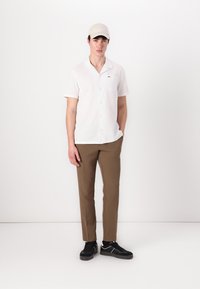 Hvit kortermet skjorte med knapper og lomme, kombinert med brune bukser og svarte sneakers. En beige cap fullfører antrekket.