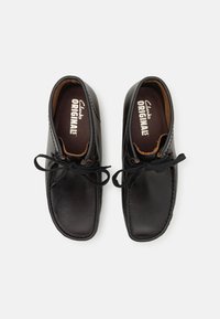 Zapatos de cuero negro con una textura suave, con punteras redondeadas, detalles de costura y cordones negros. El forro interior muestra la marca "Clarks ORIGINALS".