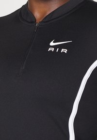 Svart sporttopp med hög krage, delvis dragkedja och vit "AIR"-logotyp. Har en vit accentlinje längs sidan. Mjukt, stretchigt tyg.