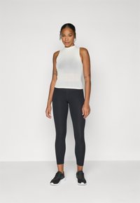 Top senza maniche bianco a costine abbinato a leggings neri e scarpe da ginnastica nere. Il top presenta un collo alto e un design testurizzato.