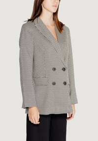Blazer doppiopetto in bianco e nero a motivo houndstooth con revers a punta, due tasche frontali e bottoni neri, realizzato in tessuto testurizzato.