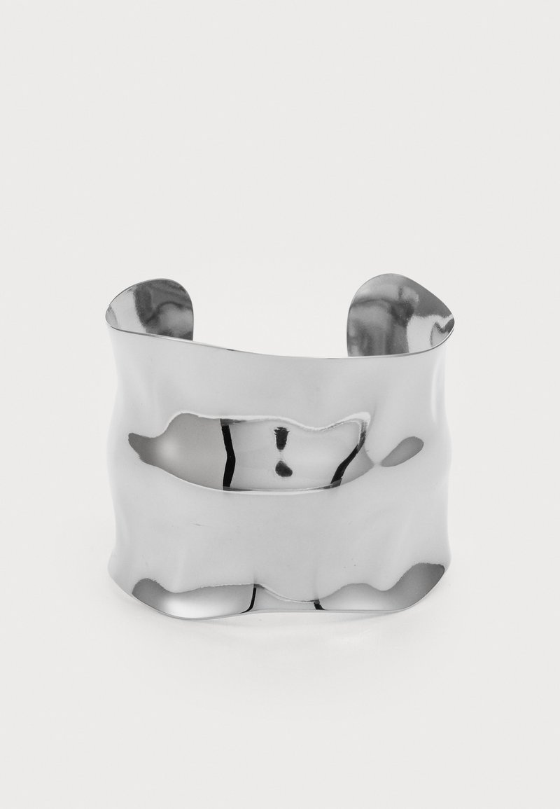 Wide silver cuff bracelet with a wavy, irregular surface and an open back, reflecting light on a plain white background.