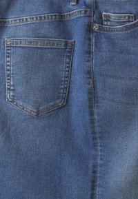 Tamno plave traperice s jednim stražnjim džepom, vidljivim šavovima i glatkom teksturom s blagim sjajem.