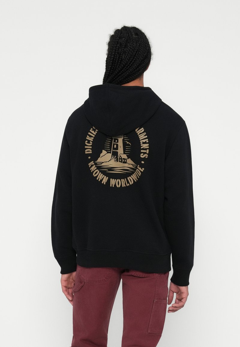 Hoodie preto com um design gráfico dourado nas costas, apresentando um farol e o texto "Dickies Garments Known Worldwide." Ajuste relaxado.