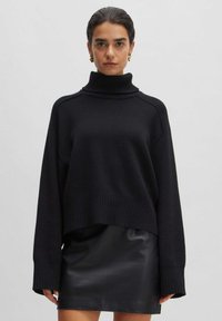 Zwarte oversized coltrui, gebreide textuur, geribde zoom en manchetten, gedragen over een zwarte leren minirok.