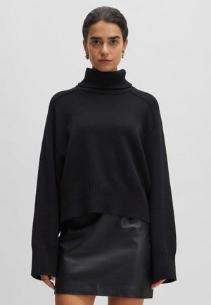 Black oversized turtleneck sweater, knit texture, ribbed hem and cuffs, worn over a black leather mini skirt.