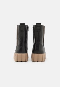 Botas de tobillo de cuero negro con paneles laterales de malla texturada, suelas de plataforma beige gruesas y cremalleras en la parte trasera para facilitar el uso.