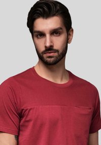 Rød bomulds T-shirt med et tekstureret overpanel, rund halsudskæring og en lille lomme på venstre bryst. Glat stof med korte ærmer.