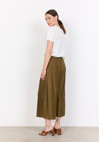 White short-sleeve shirt paired with olive green pleated culottes and brown heeled sandals, seen from a slight back angle.