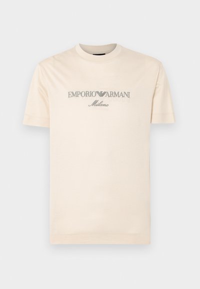 Cream cotton t-shirt with short sleeves, featuring embossed "EMPORIO ARMANI" and "Milano" text in grey across the chest. Round neckline.