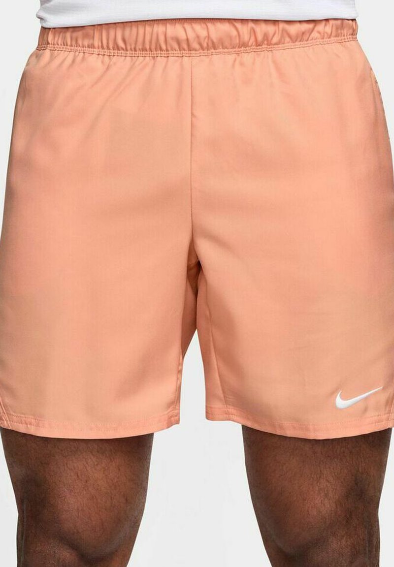 Persikofärgade träningsshorts med elastiskt midjeband och vitt Nike-logotyp på nedre högra sidan. Slät tyg, knä-lång design.