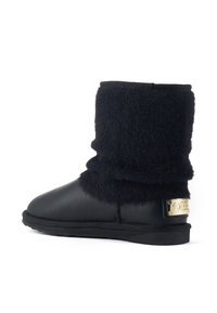 Bottines en cuir noir avec une tige douce et noire en peluche et une plaque logo dorée à l'arrière, dotées d'une semelle en caoutchouc plate.