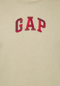 Sudadera beige con logo "GAP" bordado en relieve en tonos rojo oscuro y rojo claro. Textura suave con cuello y puños acanalados.