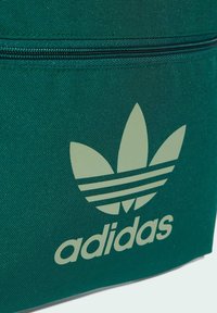Borsa in tela verde con un logo Adidas verde chiaro caratterizzato da tre forme simili a foglie e tre strisce orizzontali sopra il nome del marchio.