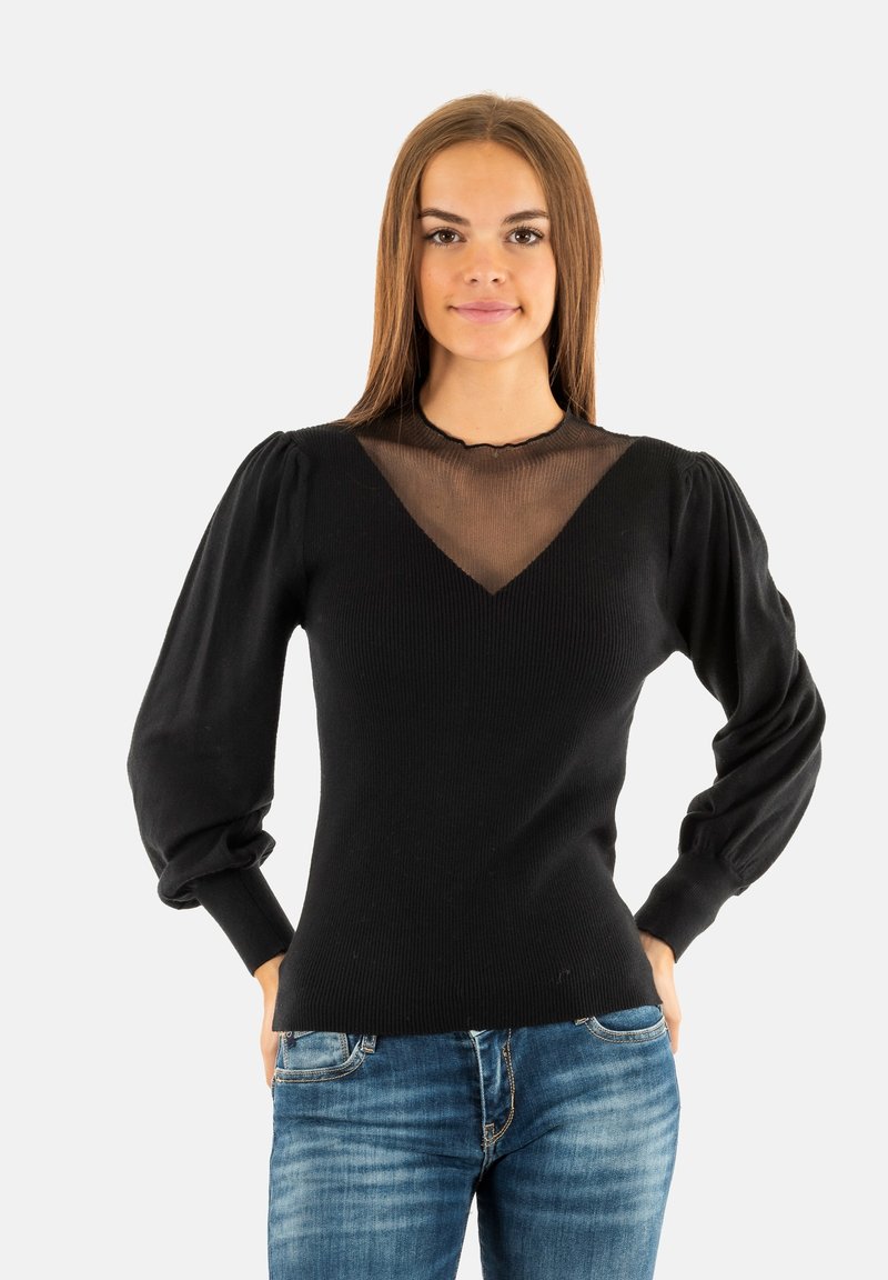 Maglione nero a coste con scollatura a V in mesh trasparente e maniche lunghe a sbuffo, abbinato a jeans di denim blu. Texture liscia e design aderente.